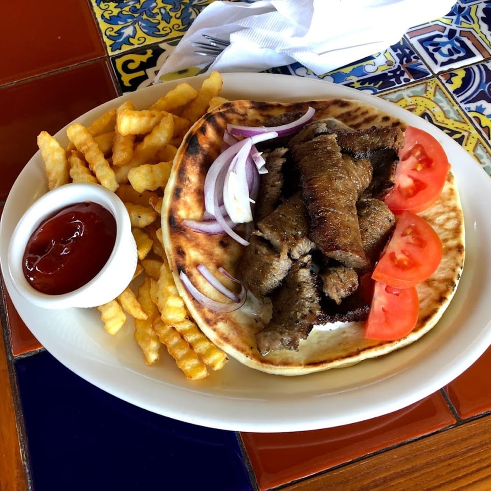 Gyro with sliced meat, tomatoes, red onions, and fries with ketchup on a white plate.