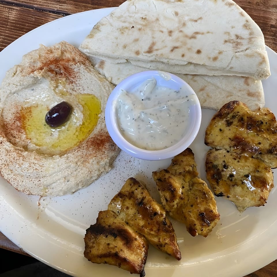 Mediterranean platter with hummus, pita bread, grilled chicken, and a side of tzatziki sauce.