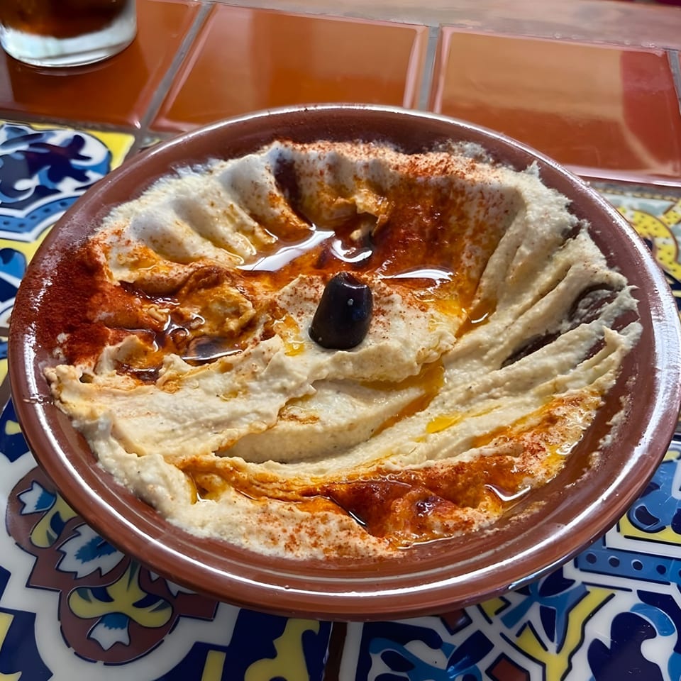 Creamy hummus drizzled with olive oil and paprika, topped with a single black olive.