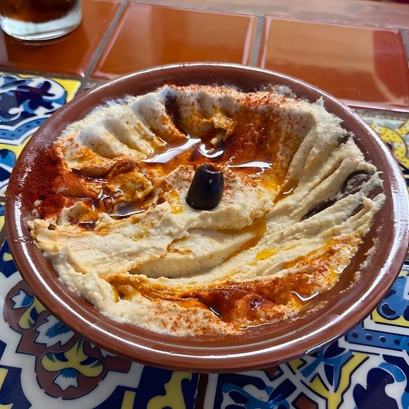 Creamy hummus drizzled with olive oil and paprika, topped with a single black olive.