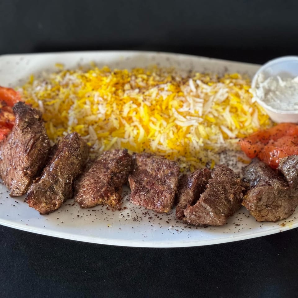 Mediterranean grilled beef kebabs with saffron rice, roasted tomatoes, and a side of sauce.