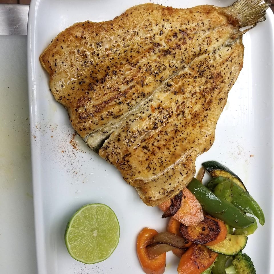 Grilled Mediterranean fish with roasted vegetables and a lime wedge on a white plate.