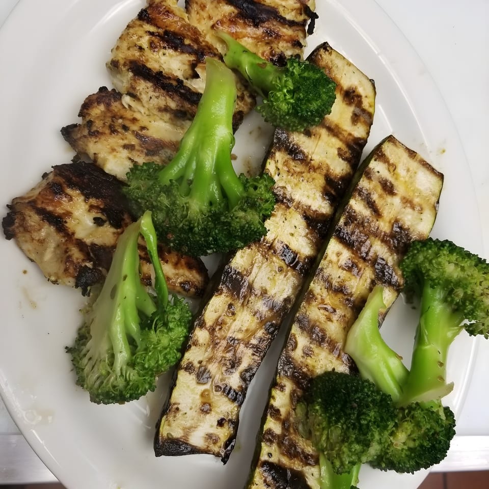 Grilled chicken, zucchini, and broccoli florets arranged on a white plate.