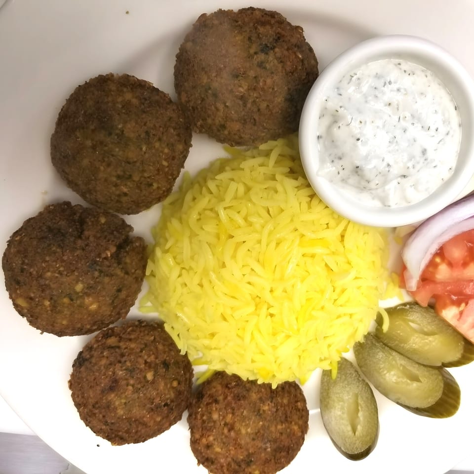 A Mediterranean falafel plate with five falafel patties, yellow rice, tzatziki sauce, pickles, and tomatoes.